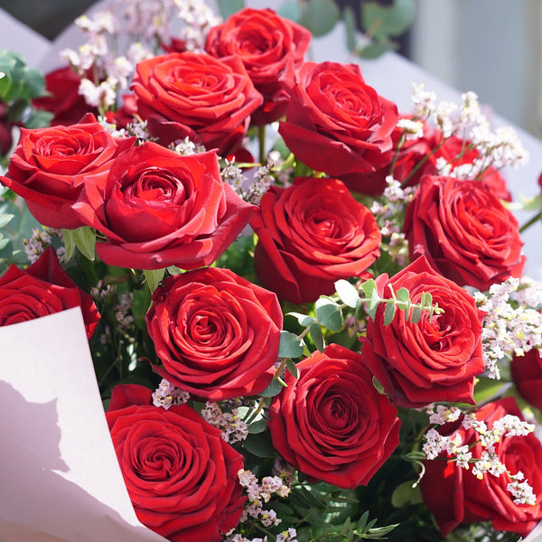 Introducing the Red Romance Rose Bouquet by Wild About Flowers: a luxurious mix of vibrant red roses, delicate white flowers, and lush green foliage. Wrapped in light pink paper, this romantic bouquet is perfect for local delivery and a gesture of love.