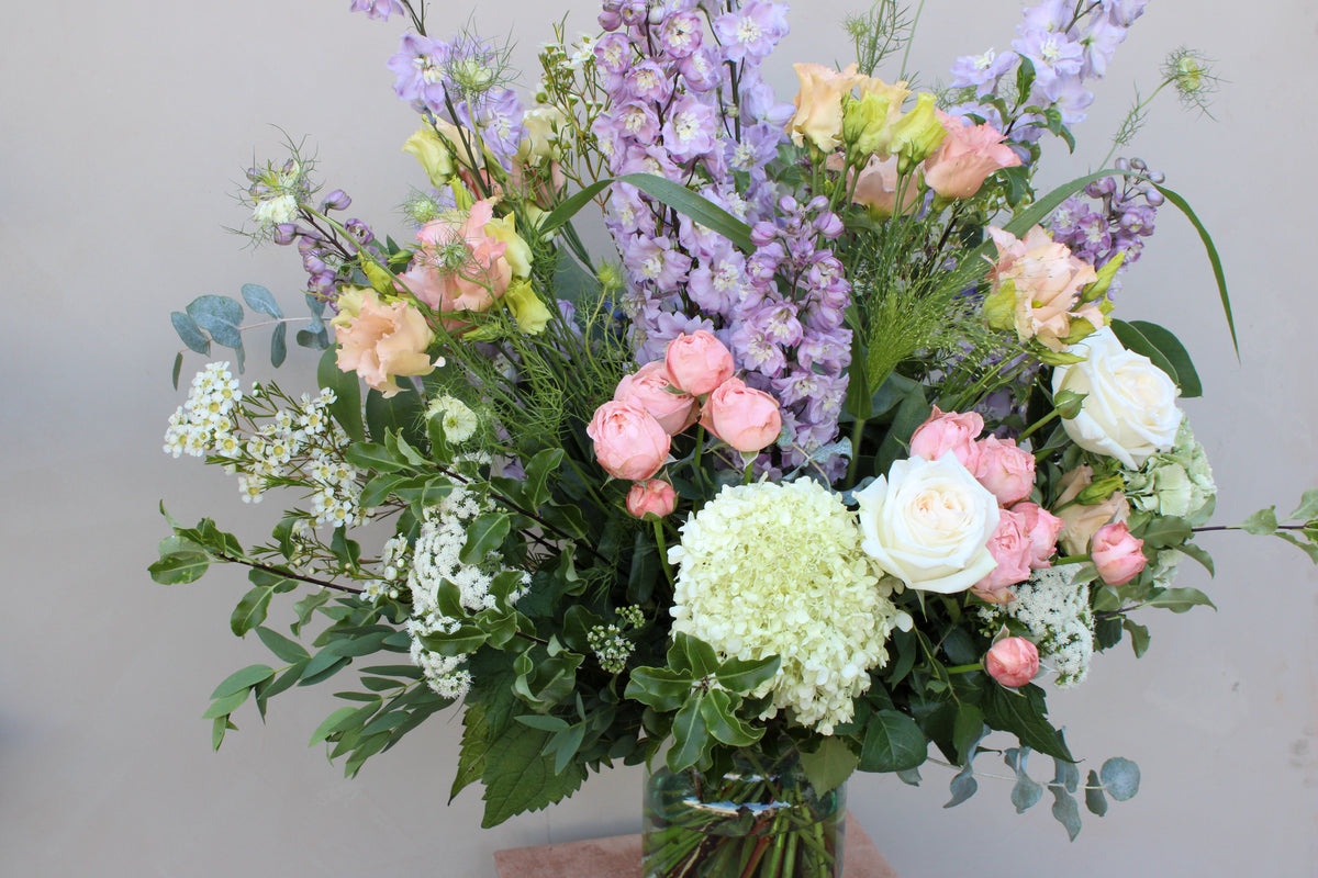 Introducing the Gorgeous Bouquet from Wild About Flowers, featuring fresh flowers in radiant shades of pink, white, and purple, arranged elegantly in a glass vase. Skilled florists have expertly combined roses, hydrangeas, and other assorted blooms with lush greenery and delicate white blossoms. Ideal for any setting against a plain, light-colored background.