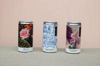 The Wild About Flowers Premium Wine Gift Set features three elegantly designed cans against a soft pink background: one with a floral pattern, another with a blue toile design, and a third with a purple abstract motif, showcasing award-winning Malbec, Sauvignon Blanc, and Lucarne Rosé wines.