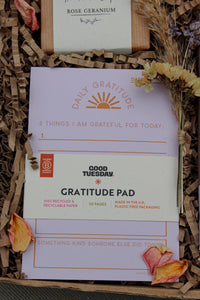 A purple "Good Tuesday" gratitude pad in the Wix Galentine's Gift Box sits on shredded paper, inviting users to list three gratitudes. Accompanied by dried flowers and rose geranium soap, it's perfect for a cozy night or friendship celebration.