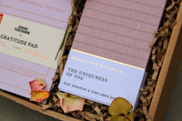 A lavender-hued Galentine’s Gift Box from Wix contains Banks-Lyon Botanical's "The Uniqueness of You" rose geranium and sunflower bath product, elegantly surrounded by dried rose petals and multicolored gratitude pads, perfect for a cozy night in.