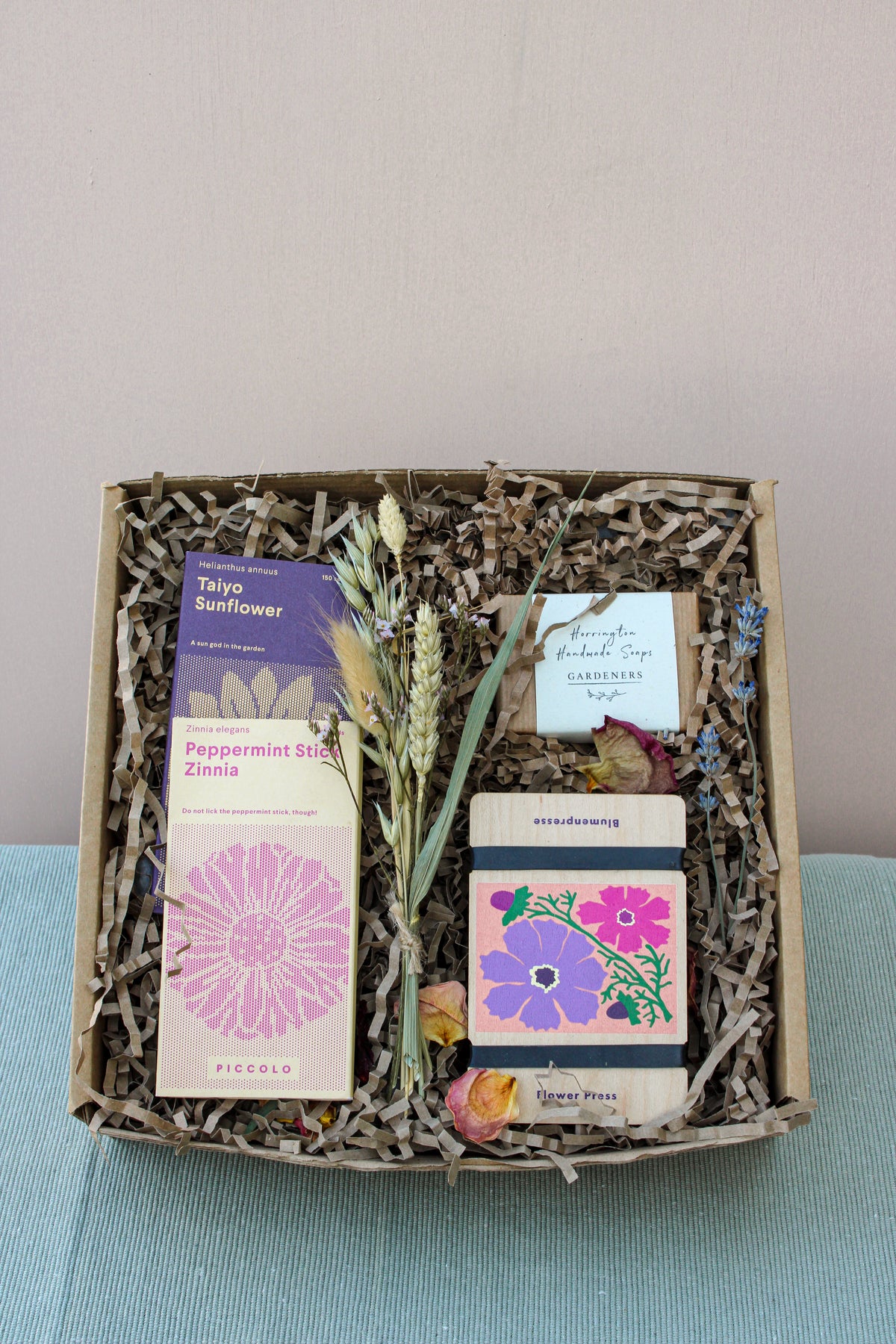 Introducing the Wild About Flowers Flower Power Gift Box: an enchanting eco-friendly gift for gardening enthusiasts. This box includes packets of flower seeds, gardener's hand soap, and two bars of soap. Decorated with dried flowers and filled with shredded paper packing, it makes an ideal present for nature lovers.