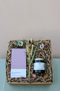 The Wild About Flowers *Peace and Quiet Gift Box* includes a luxurious rose geranium and sunflower bath bar, a "Tinder Box" candle for added ambiance, dried flowers, and natural decorative paper filler. This set is perfect for creating an at-home spa experience, all beautifully presented on a soothing light blue surface.