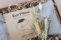 The Total Timeout Gift Box by Wild About Flowers includes a packaged eye pillow in a crinkled paper-filled box, with dried wheat stalks and small flowers for relaxation. The label depicts a face and specifies it's for hot and cold therapy.