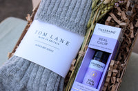 The Comfort and Calm Gift Box by Wild About Flowers includes grey Alpaca bed socks, a Tisserand Real Calm Roller Ball, and dried flowers, all beautifully presented for a soothing, cozy experience.