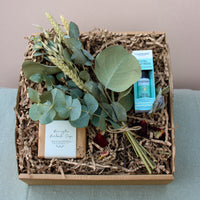 The Eucalyptus Lover Gift Box by Wild About Flowers includes a calming bar of eucalyptus soap, a Tisserand Total De-Stress rollerball infused with natural essential oils, and fresh eucalyptus leaves. Each item is thoughtfully arranged in shredded paper on a cushioned base to create the perfect relaxation gift.