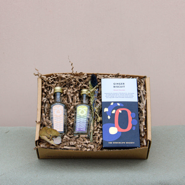 The Lovely Pair Gift Box includes two small bottles with artistic labels and a "Ginger Biscuit" chocolate bar by The Chocolate Society, all nestled in eco-friendly packaging.