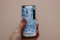A hand with gray nail polish holds a can of Sauvignon Blanc 2023, part of the eco-friendly Premium Wine Gift Set by Wild About Flowers. The can boasts blue, vintage-style illustrations on a light background.