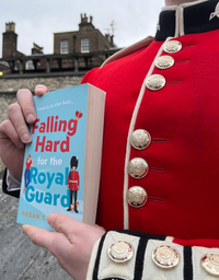 At a floral home event in front of a stone building, someone dressed in a red royal guard uniform holds the book "Falling Hard for the Royal Guard" during the Event: In Conversation—Megan Clawson | Book Reading and Q&A.