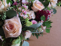 A detailed view of the 'From the Heart' Heart Design by Wild About Flowers showcases a floral arrangement with blush roses, deep red chrysanthemums, and delicate pink and white blossoms, all nestled amidst lush green foliage.