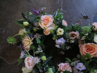 The 'From the Garden' Heart Design by Wild About Flowers showcases a beautiful arrangement of seasonal pale pink roses coupled with white and purple blooms, all elegantly set against a dark gray surface.
