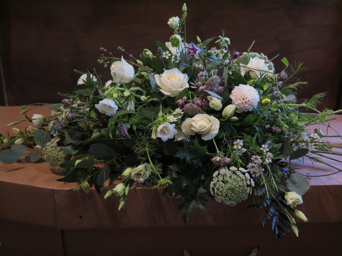 The "From the Garden" Woodland Spray by Wild About Flowers features an elegant floral arrangement of white roses and garden foliage, beautifully displayed on a wooden surface for a natural and serene effect.
