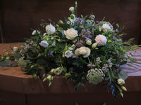 The "From the Garden" Woodland Spray by Wild About Flowers features an elegant floral arrangement of white roses and garden foliage, beautifully displayed on a wooden surface for a natural and serene effect.