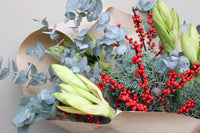 The Mulled Wine Luxury Stems by Wild About Flowers features green amaryllis buds, red berries, silvery eucalyptus, and greenery wrapped in kraft paper—an ideal Christmas floral arrangement for a festive touch.