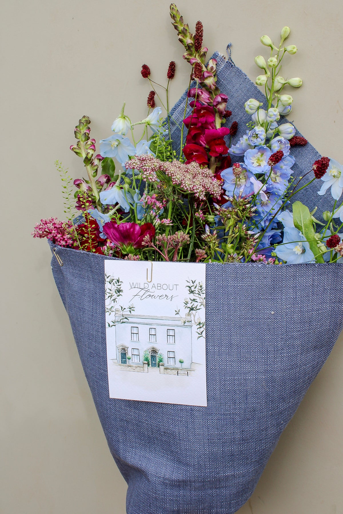 The Berry Cooler by Wild About Flowers comes wrapped in upcycled denim with a card reading "Wild About Flowers" and a shopfront illustration—a sustainable, stylish floral gift perfect for any occasion.