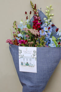 The Berry Cooler by Wild About Flowers comes wrapped in upcycled denim with a card reading "Wild About Flowers" and a shopfront illustration—a sustainable, stylish floral gift perfect for any occasion.
