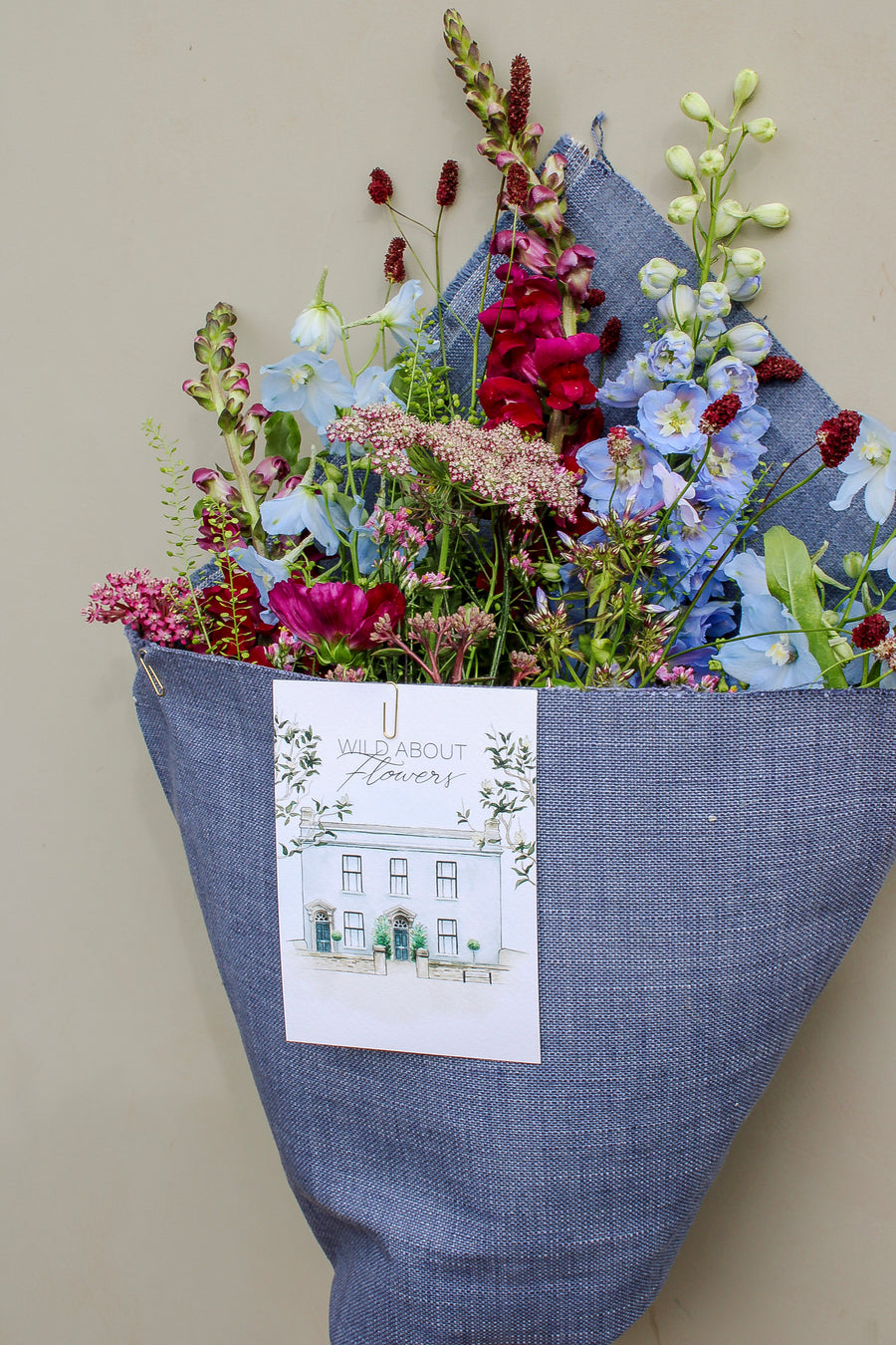 The Berry Cooler by Wild About Flowers comes wrapped in upcycled denim with a card reading "Wild About Flowers" and a shopfront illustration—a sustainable, stylish floral gift perfect for any occasion.