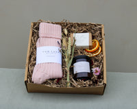 Wild About Flowers’ Winter Warmers Gift Box includes cozy pink socks, a soap bar, strawberry jam, dried orange slices, and a small dried flower bouquet, all in shredded paper.
