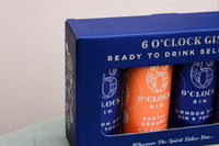 A close-up of the 6 O'Clock Gin box by Wild About Flowers reveals a selection of handcrafted gin cocktails. The blue box showcases cans, including an "Exotic Orange Gin & Tonic" and a "London Dry Gin & Tonic.