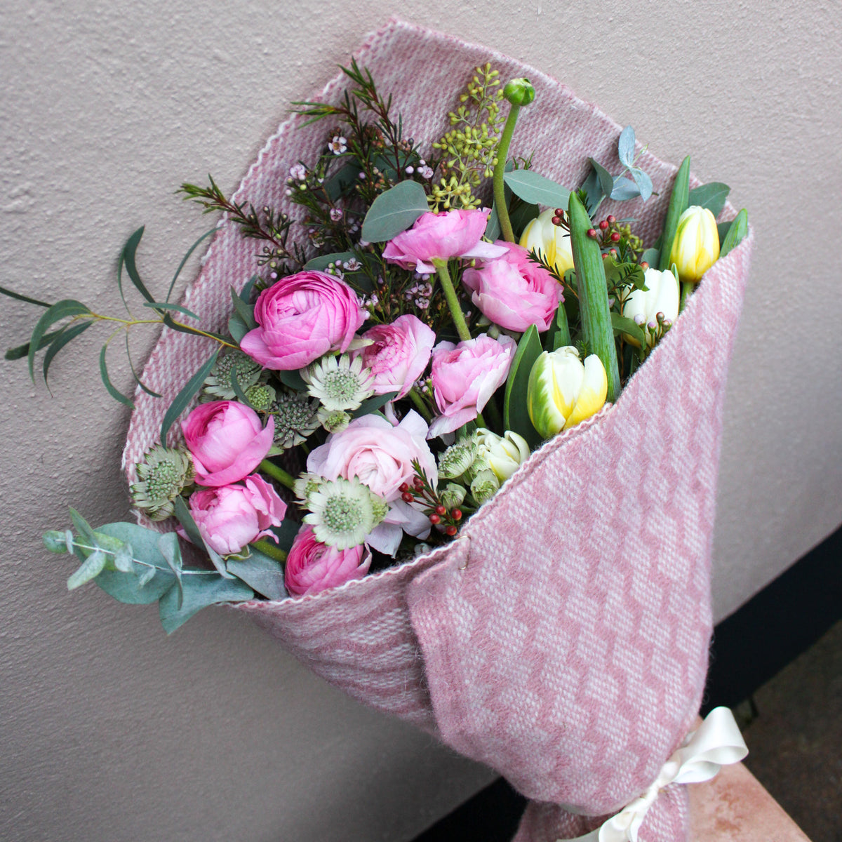 The ‘Armful of Love’ Valentines wrap by Wild About Flowers features pink and white ranunculus and tulips, beautifully wrapped in a pink patterned cloth and tied with a white ribbon—ideal for gifting or delivery.