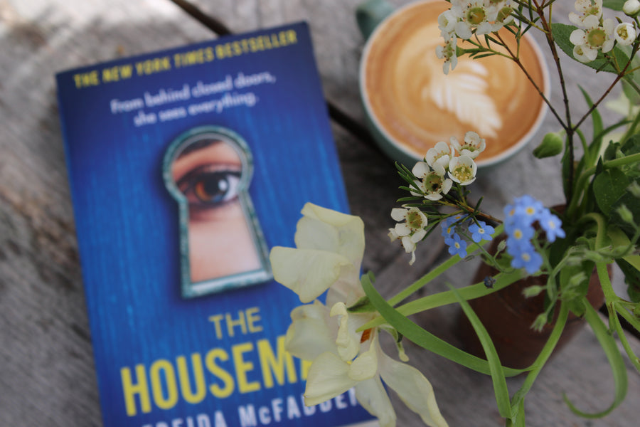 Close up of book cover The Housemaid on a table with flowers and coffee
