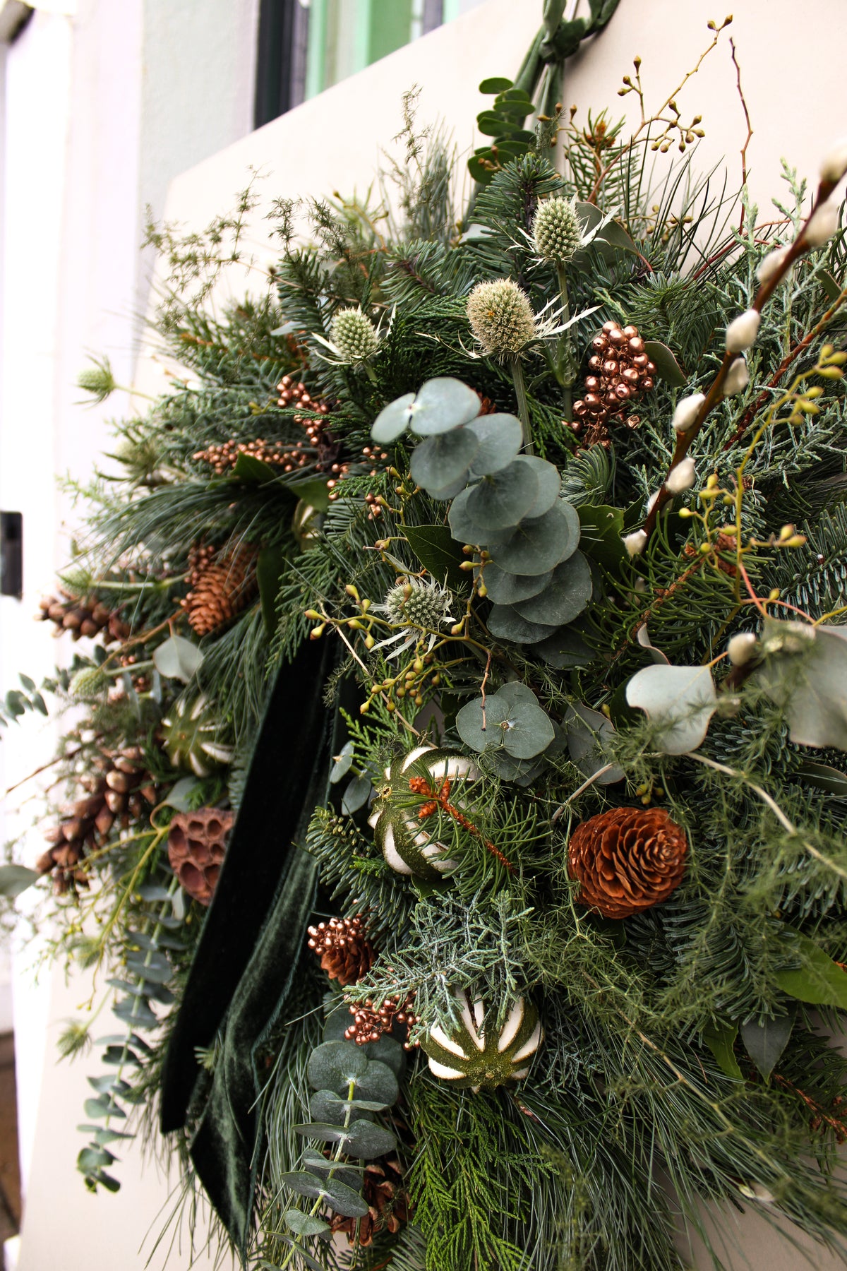 Decorative wreath with greenery, pinecones, and eucalyptus on a white wall.