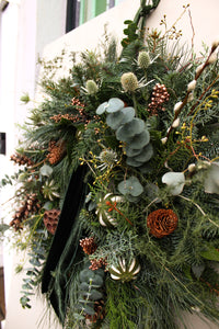 Decorative wreath with greenery, pinecones, and eucalyptus on a white wall.