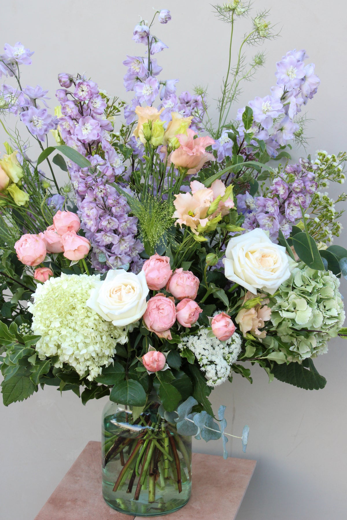 The "Gorgeous bouquet" by Wild About Flowers showcases a lush arrangement of fresh white roses, pink peonies, green hydrangeas, and delicate purple flowers accented with greenery in a clear glass vase, creating a vibrant and elegant floral display crafted by skilled florists.