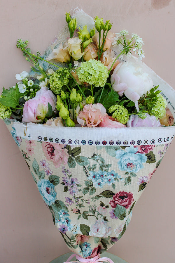 The Peony Floral Wrap by Wild About Flowers features pastel seasonal flowers, including peonies and green hydrangeas, wrapped in a limited edition summer fabric with pink and blue blooms on beige.