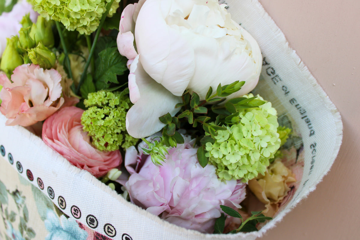 A close-up of Wild About Flowers' Peony Floral Wrap, filled with assorted seasonal blooms in white, pink, and green with lush greenery, set against a light background.