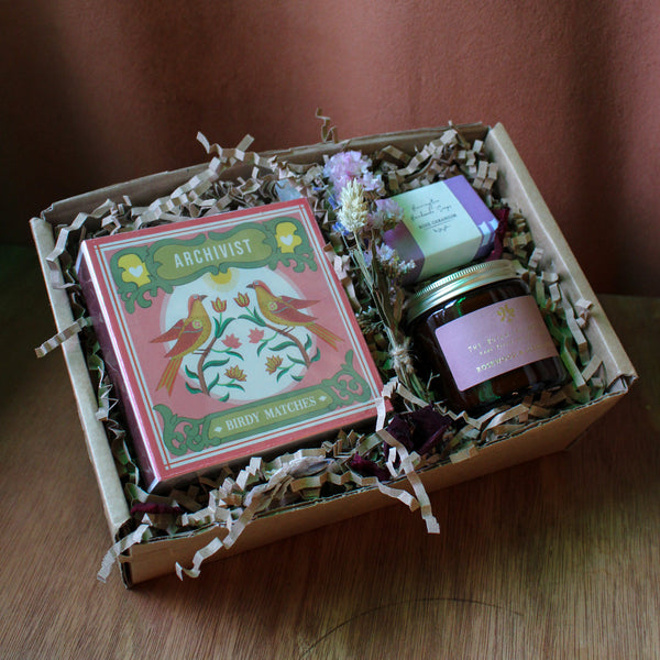 Gift box with Archivist bird matches, candle, and other items on a wooden surface.
