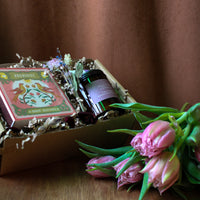 Archivist matches, candles, dried florals in a gift box with and pink tulips on a wooden surface with a brown background