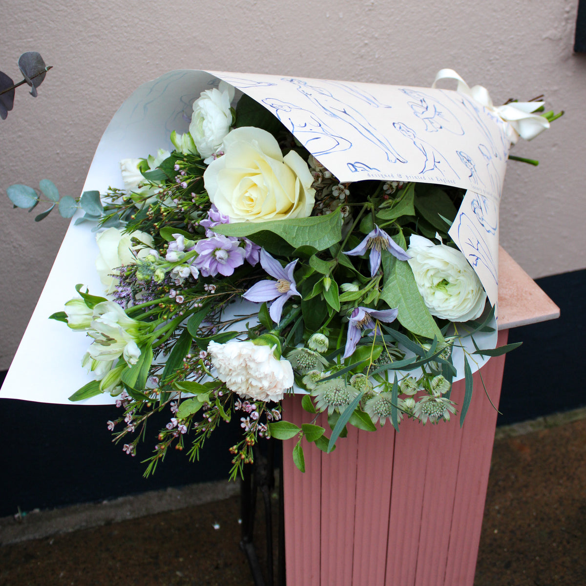 Bouquet of flowers wrapped in paper on a pink surface with a neutral background