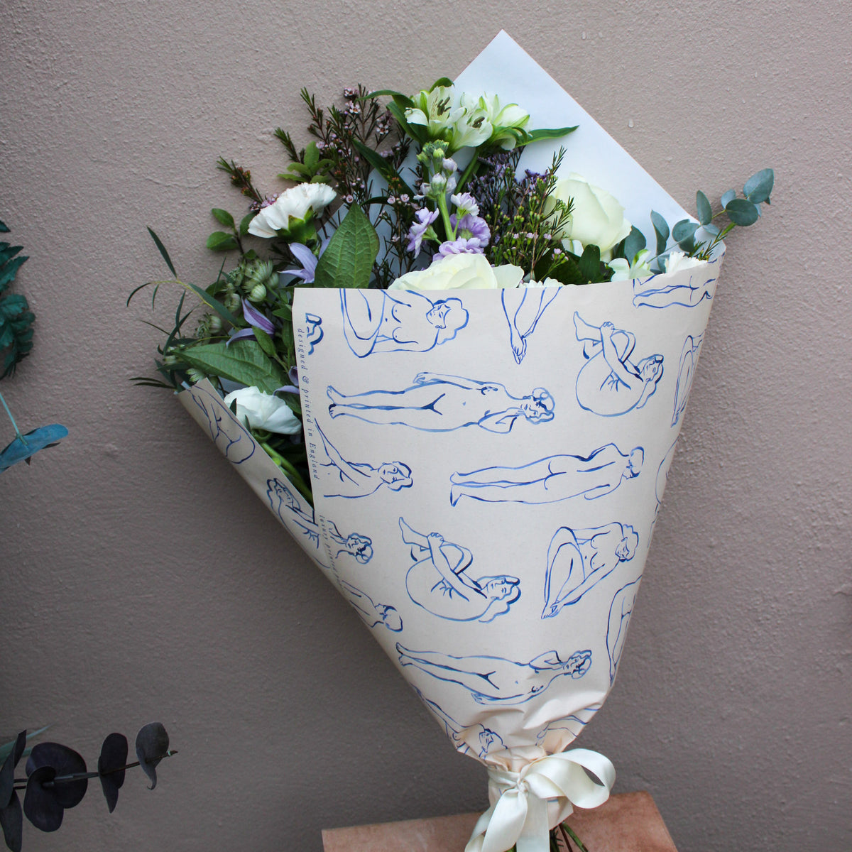 Bouquet of flowers wrapped in paper with blue line drawings on a plain background