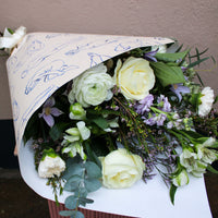 Bouquet of flowers wrapped in paper with blue writing on a neutral background