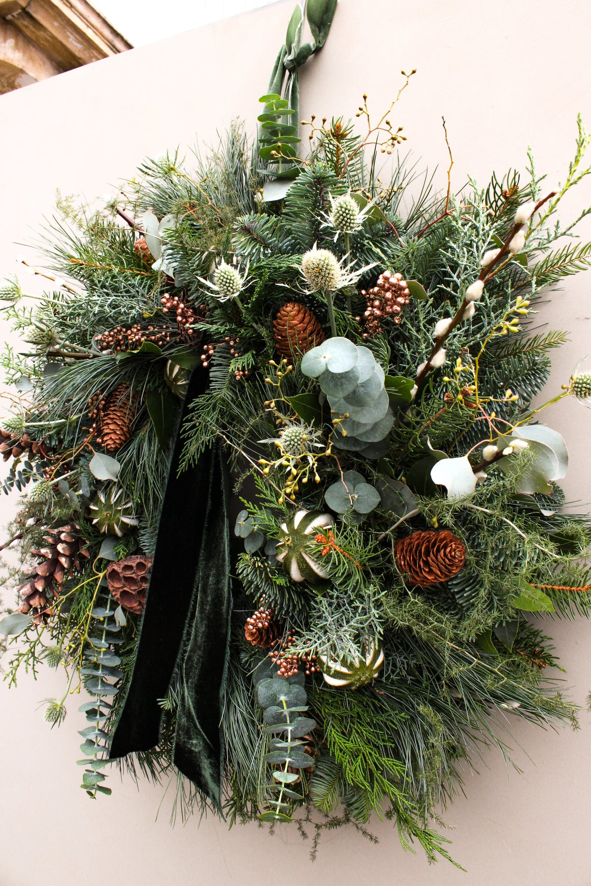 Christmas wreath with greenery, pinecones, and white berries on a plain background