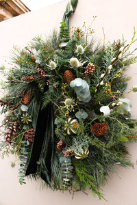 Christmas wreath with greenery, pinecones, and white berries on a plain background