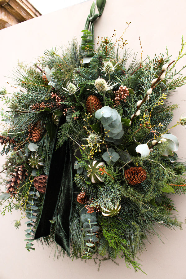 Christmas wreath with greenery, pinecones, and white berries on a plain background