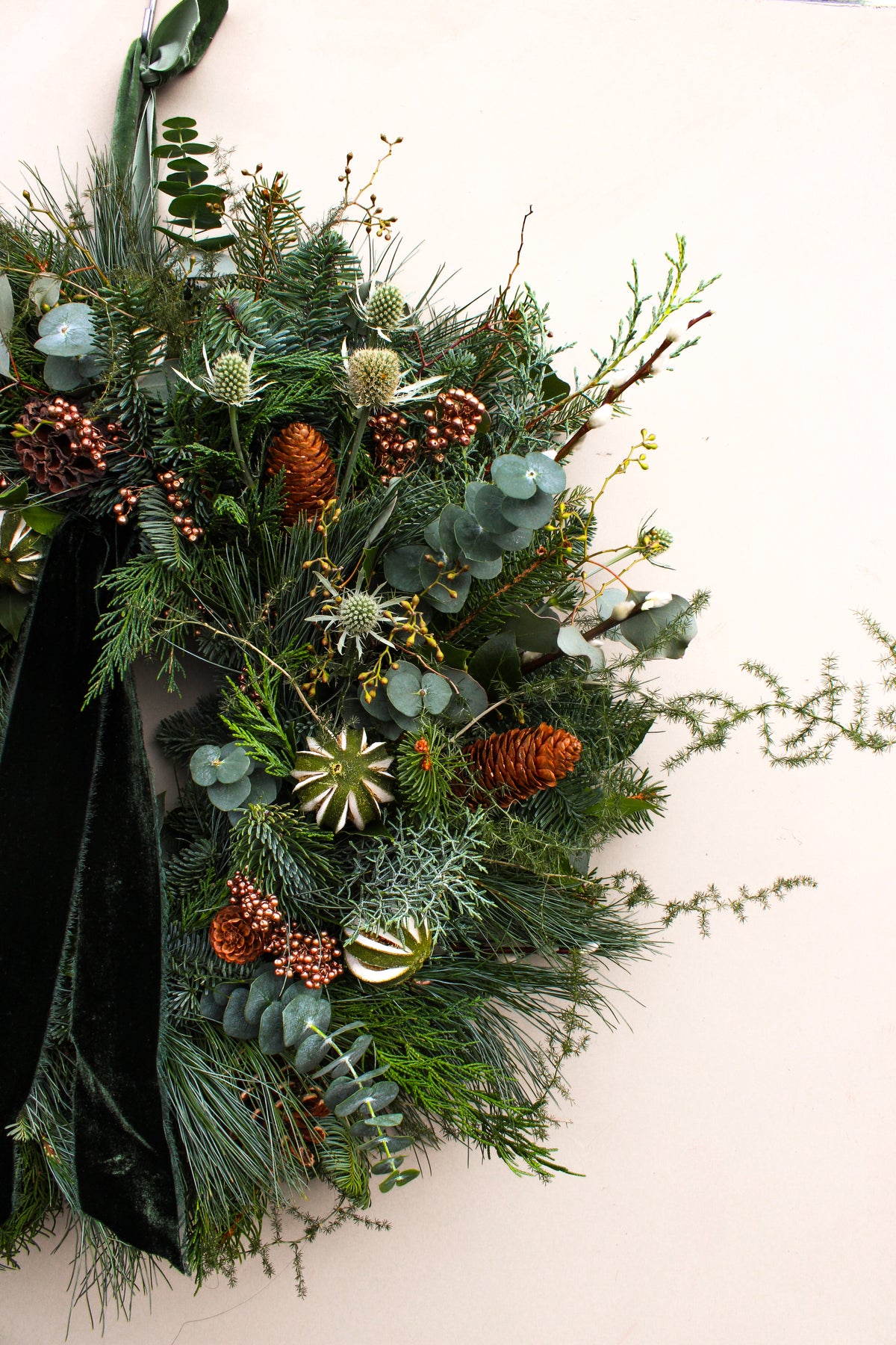 Decorative wreath with greenery, pinecones, and ribbons on a white background