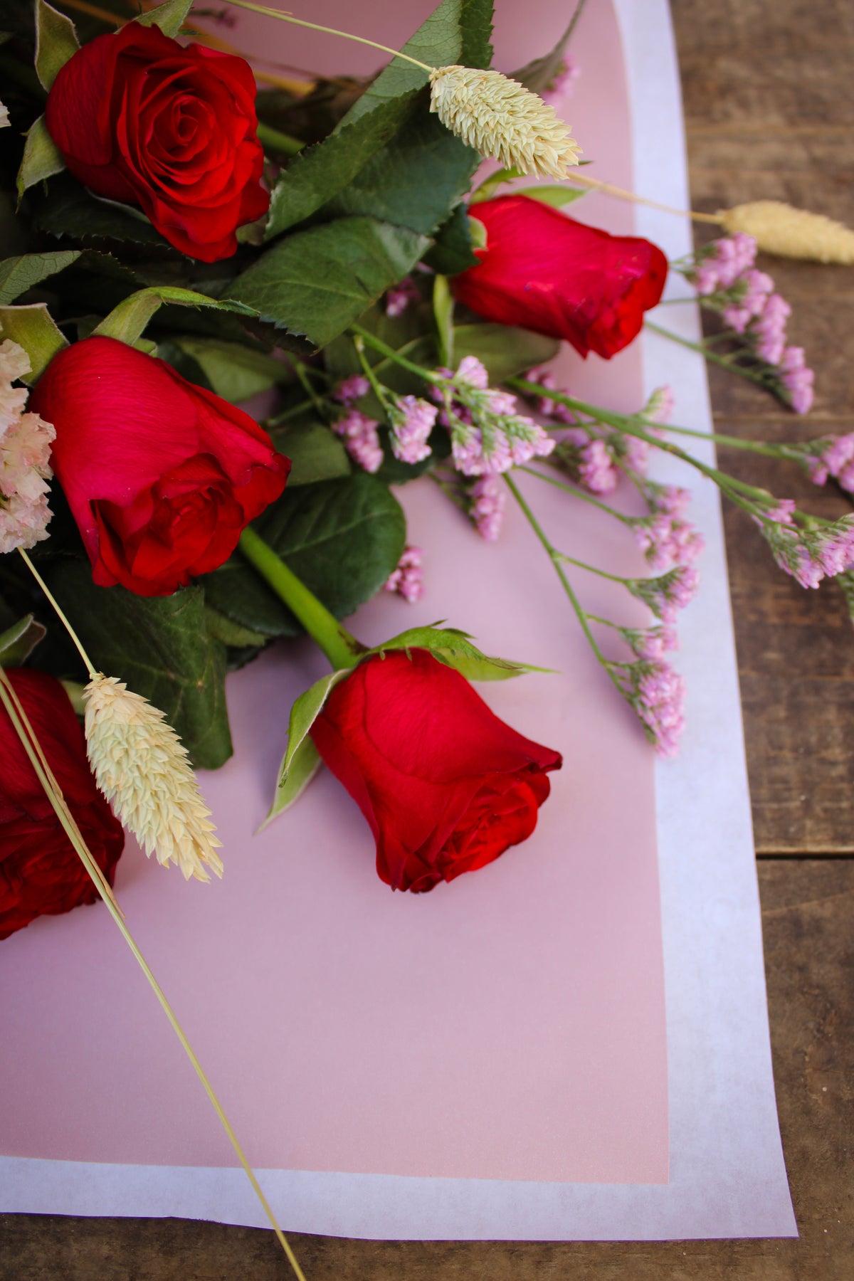 The "Early (love) bird" by Wix features a stunning design of rich red roses and soft pink blooms arranged on light pink wrapping paper atop a wooden surface, showcasing the delicate petals' soft contrast against the deep hues of red roses.