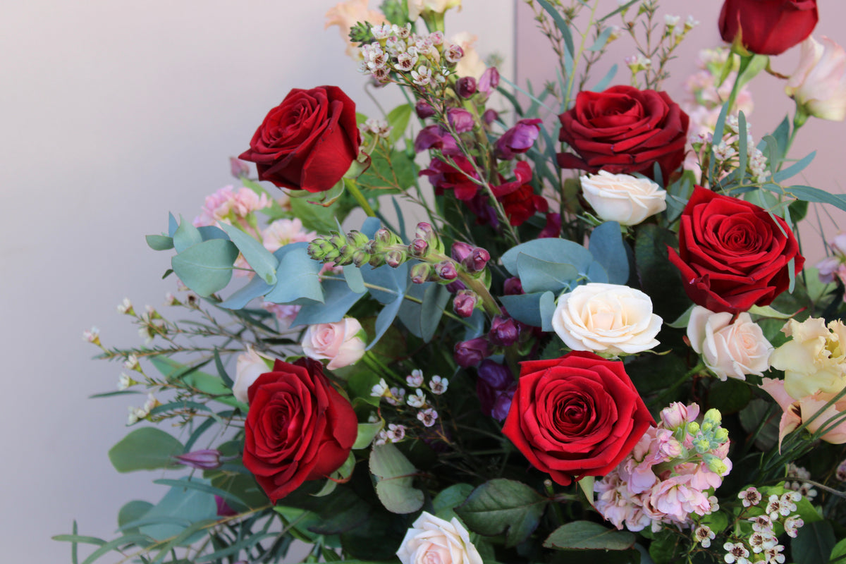 The Valentine's Day Blooms by Wild About Flowers is a vibrant bouquet with red roses, white and pink flowers, and assorted greenery in a vase. Delicate small blossoms enhance the lush display—perfect for a romantic gesture.