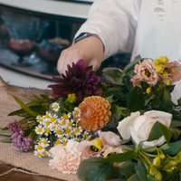Person arranging a bouquet of flowers on a table.