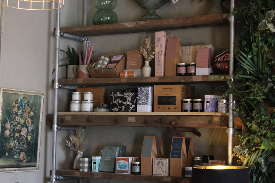 Rustic wooden shelves displaying candles, gift boxes and homeware items inside a flower shop