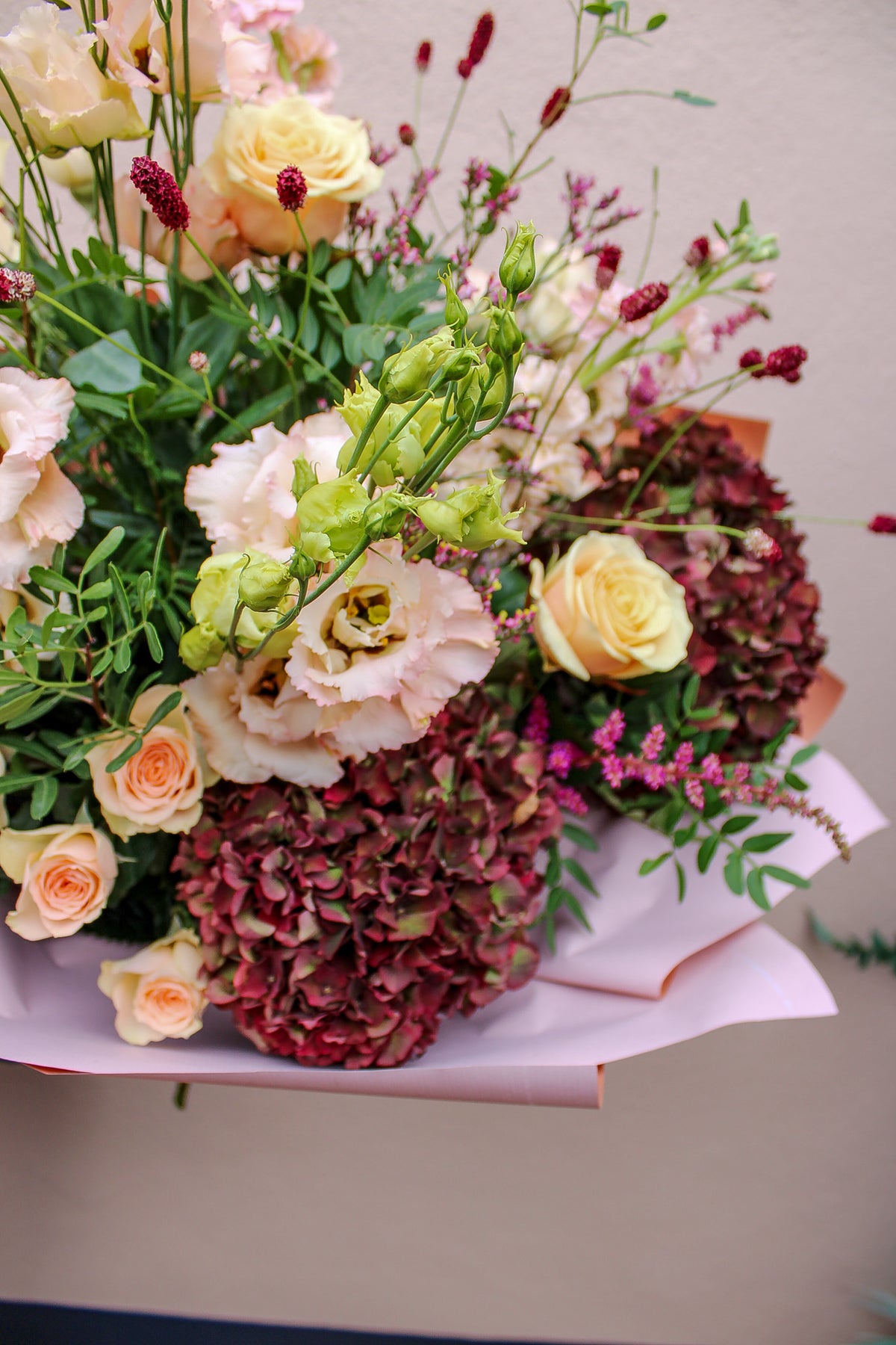 The Pecan Pie bouquet by Wild About Flowers features pale peach roses, white lisianthus, burgundy hydrangeas, and greenery in pink wrapping—perfect for autumn flower delivery or hand-tied flowers in Keynsham.