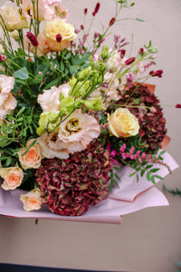 The Pecan Pie bouquet by Wild About Flowers features pale peach roses, white lisianthus, burgundy hydrangeas, and greenery in pink wrapping—perfect for autumn flower delivery or hand-tied flowers in Keynsham.