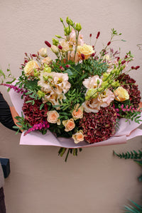 The Pecan Pie bouquet by Wild About Flowers features pale roses, light pink lisianthus, burgundy hydrangeas, and greenery in light pink wrap—ideal for hand-tied flowers in Keynsham.