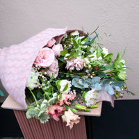 The ‘Strawberry Kisses’ Valentine’s Flower Wrap by Wild About Flowers features pink and white roses, elegantly wrapped in soft pink cloth and displayed on a matching stand for a romantic gift.