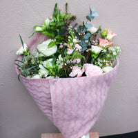 Wild About Flowers’ ‘Strawberry Kisses’ – a romantic Valentine’s flower wrap with white roses and pink carnations in textured pink cloth, perfect as a bouquet or for local delivery, set against a light gray background.