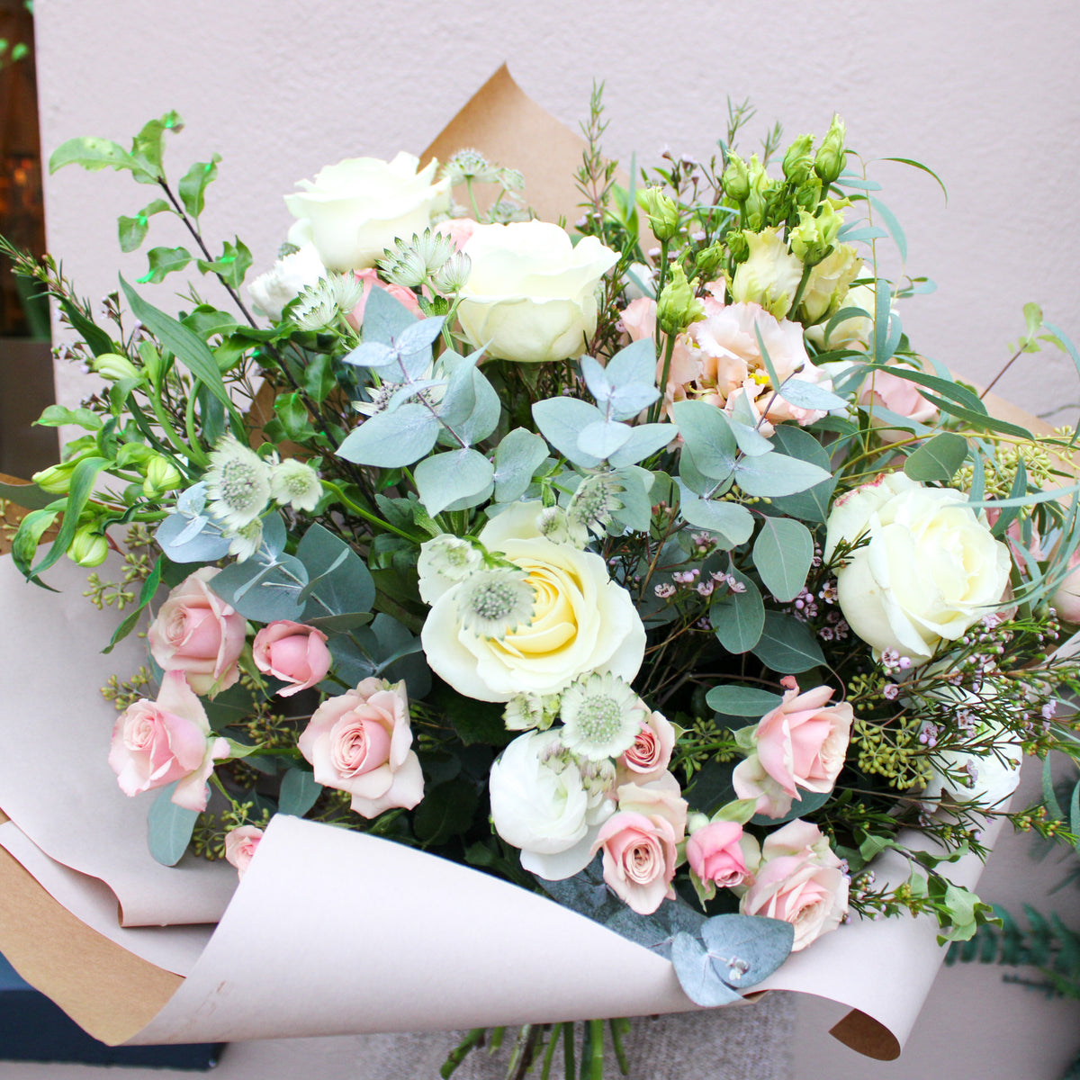 The 'Sweet Blossom' Pink and White Fresh Flower Bouquet by Wild About Flowers features premium white roses, light pink blooms, and eucalyptus, hand-tied with greenery—an ideal Valentine's Day gift.