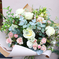 The 'Sweet Blossom' Pink and White Fresh Flower Bouquet by Wild About Flowers features premium white roses, light pink blooms, and eucalyptus, hand-tied with greenery—an ideal Valentine's Day gift.
